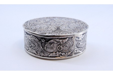 Caixa de comprimidos em prata relevada com motivos florais de forma redonda e tampa basculante.